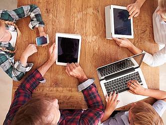 people using multiple devices - laptop, tablets, phone, while sitting around table